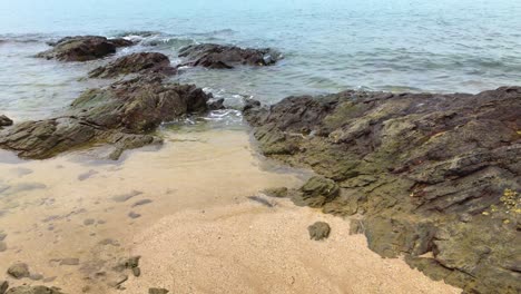 A-small-water-stream-cuts-through-the-rocks-on-the-beach,-a-sunny-day,-background-of-sea-waves