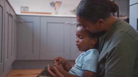 american army mother in uniform home on leave hugging son sitting on floor in family kitchen