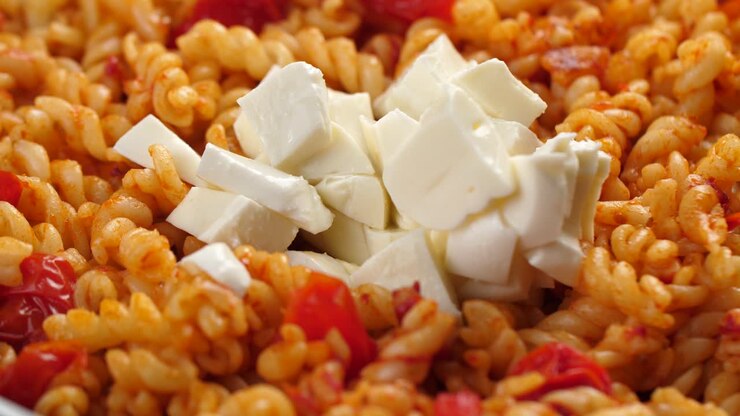 Primo piano al rallentatore di pezzi di mozzarella aggiunti a fusilli cotti con salsa di pomodoro in padella.