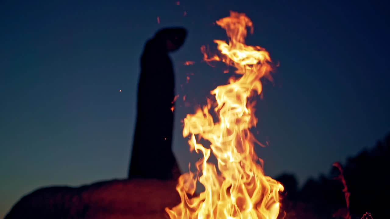 Witch on Halloween Day. Witch in cloak with hood near the fire in forest