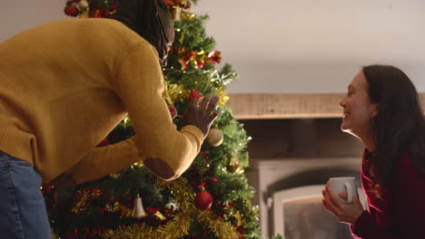 Feliz-Pareja-Diversa-Tomando-Café-Y-Decorando-El-árbol-De-Navidad-En-Casa,-Cámara-Lenta