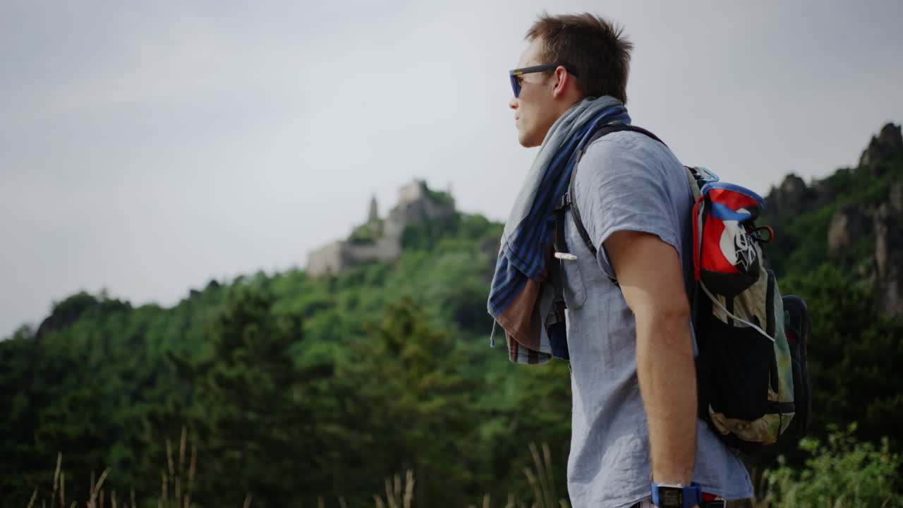 man looking over green mountain landscape, Burgruine D&uuml;rnstein castle in the background, hiking trail, hills valley, hike trekking route Austria outdoor walking route, male person taking a break, rest