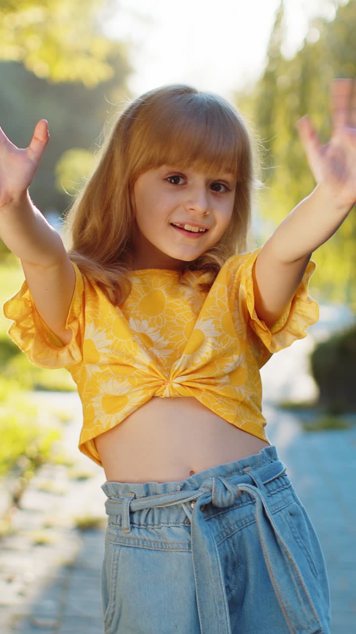Niña sonriendo amigablemente a la cámara agitando las manos hola hola saludo o bienvenido a la calle City Park