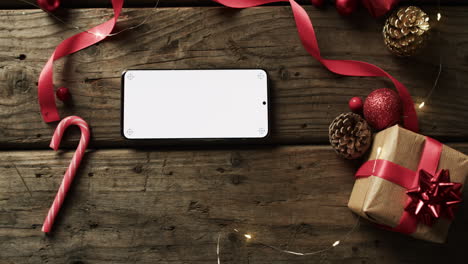 a smartphone with a blank screen lies among holiday decorations on a wooden surface