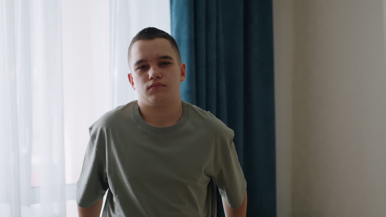 Young boy standing shirtless near window holding cloth preparing to dress in casual outfit with soft daylight creating natural scene of childhood routine and morning lifestyle
