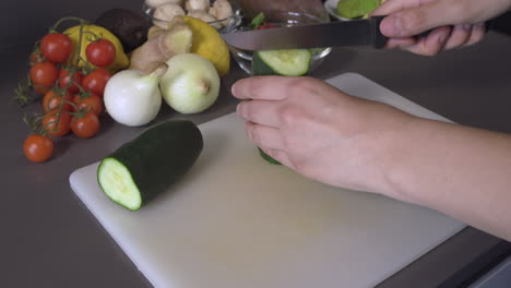 cutting a fresh cucumber in the chopping board for salad. variety of fruits and vegetables on the side.  - close up shot