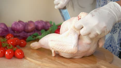 mujer cortando pollo crudo en una tabla de madera en la cocina