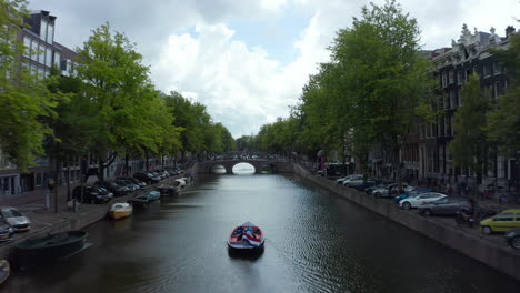 Establisher-over-Amsterdam-Canal-with-Boat-and-Dutch-Flag-waving-in-wind,-backwards-Aerial