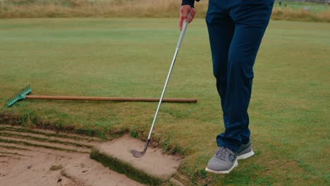 male golfer hits sand off shoe in green side pot bunker on ireland links golf course in slow motion