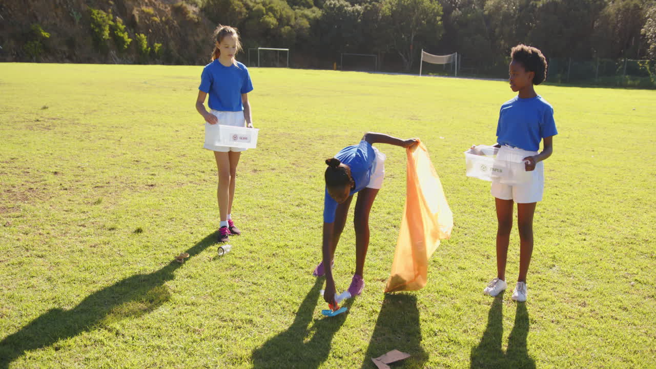 Picking up trash, girls in school uniforms cleaning up field together