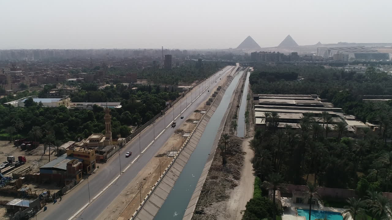 pista de disparo aéreo hacia fuera y subiendo para las pirámides de egipto en giza en el fondo de una rama del río nilo en el primer plano rama maryotya que muestra las tierras agrícolas y la vegetación