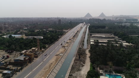 Aerial-Shot-Track-out-and-rising-up-for-The-Pyramids-of-Egypt-in-Giza-in-the-background-of-a-branch-of-the-River-Nile-in-the-foreground-Maryotya-branch-showing-the-agricultural-lands-and-greenery