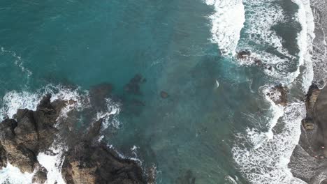 aerial view of a black sand beach with ocean waves breaking on the shore