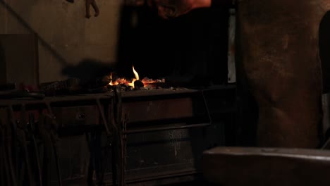 Mid-section-of-blacksmith-heating-iron-rod-in-fire