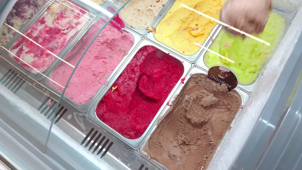 Hand Scooping Chocolate Ice Cream from Colorful Gelato Display Case