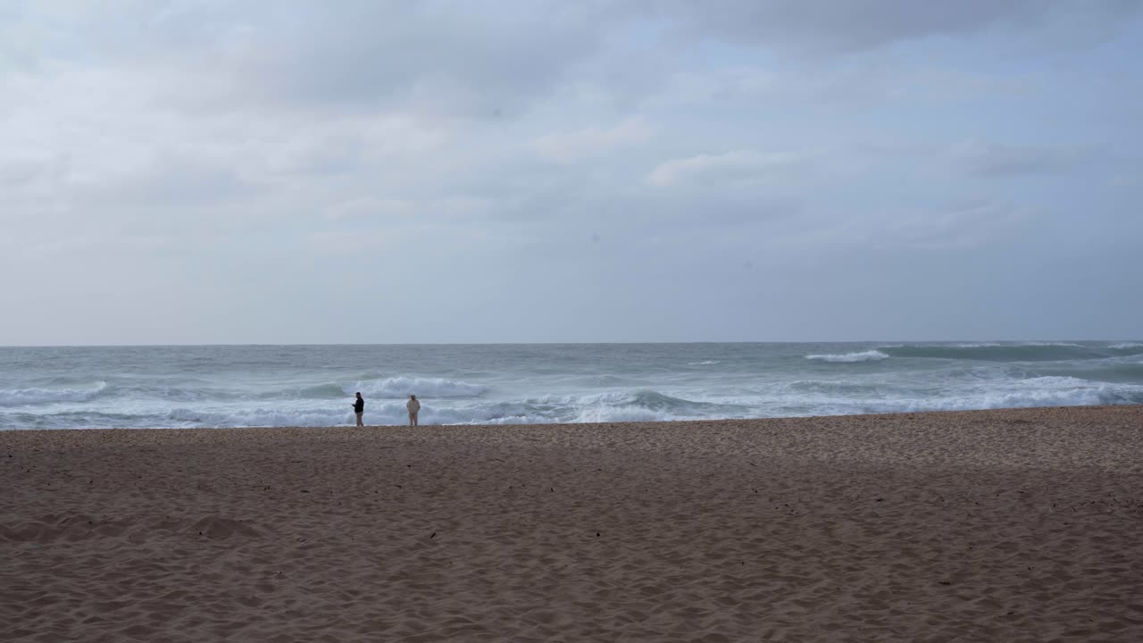 turistas caminando por una playa con violentas olas marinas que se estrellan en praia da adraga en portugal