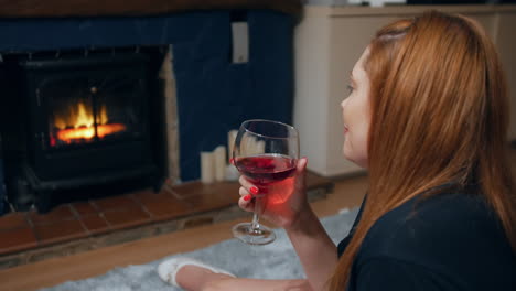 a woman with a glass of wine sitting in front of a fireplace watching a fire in a living room