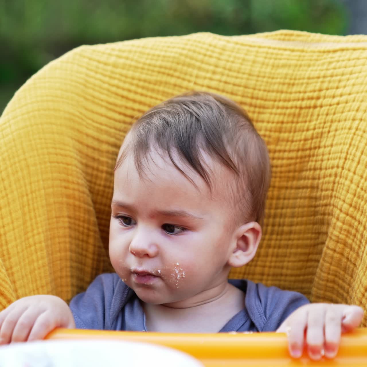 Sweet little baby boy sitting in the yellow chair. Cute kid with smudgy face eating porridge from spoon. Close up