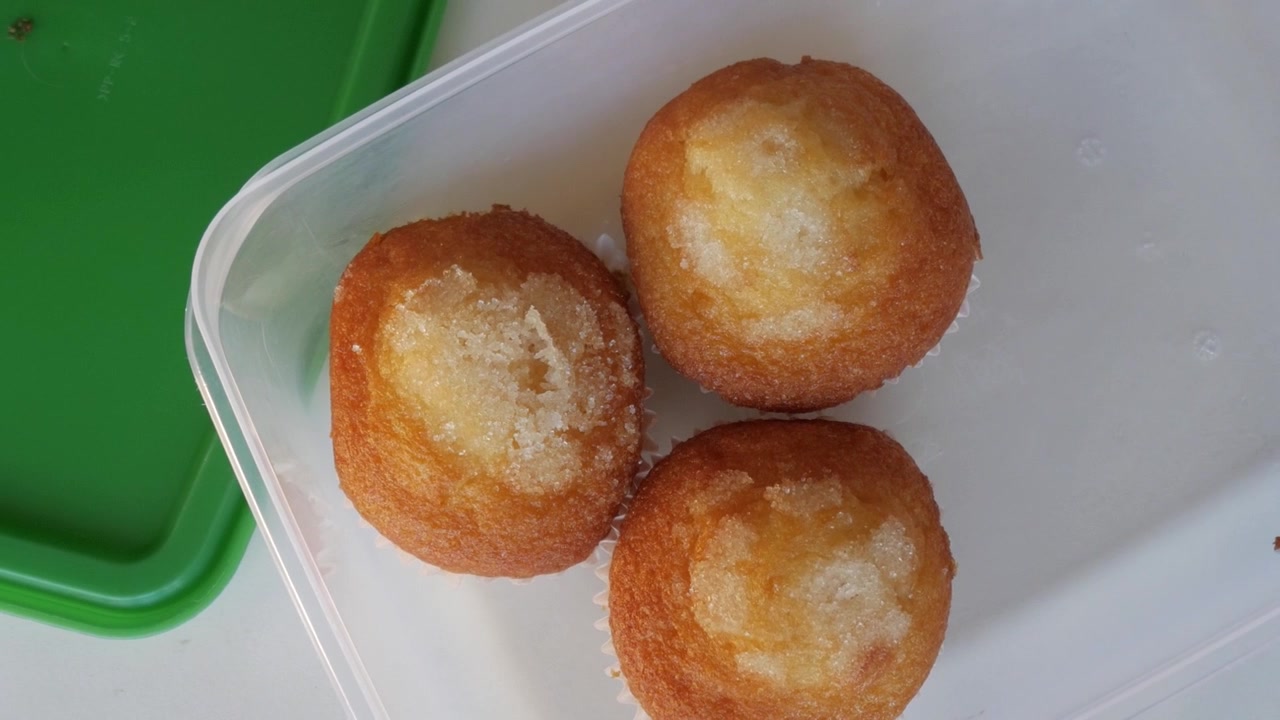 Primo piano di tre muffin ricoperti di zucchero in un contenitore di plastica