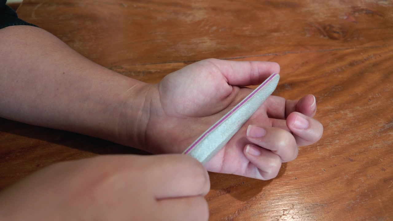 Mani femminili che usano una lima per unghie durante un trattamento di manicure e benessere di bellezza al chiuso.