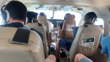 pov passenger: six caucasian people sitting in small airplane wearing face masks flying together in small cockpit, covid-19 pandemic, handheld close up behind