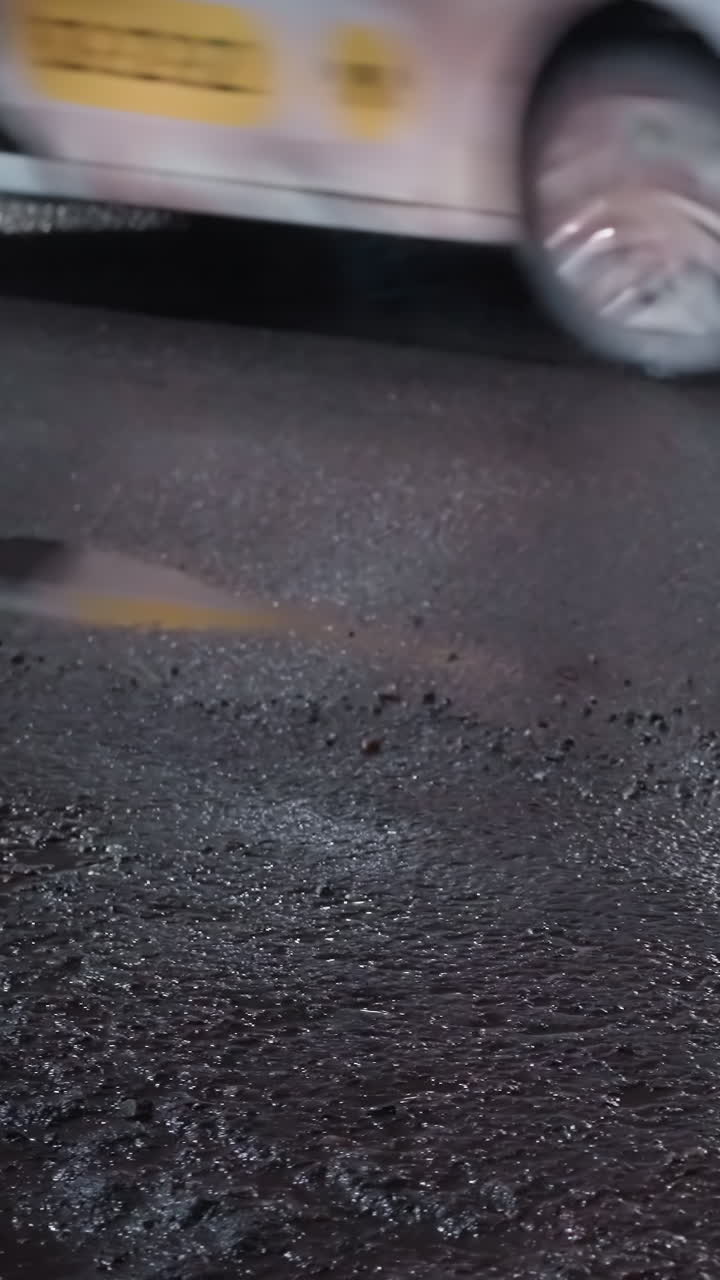 밤에 은 도로의 클로즈업 뷰, 반이는 표면에 빛의 반사와 두 개의 색 자동차가 지나가고 있습니다.