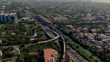 Drone shot capturing densely populated city with metro approaching station and vehicles on roads during daytime.