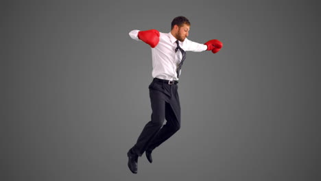 businessman in boxing gloves jumping and punching on grey background