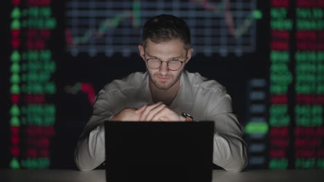 MUzhchina-broker-investor-in-glasses-looks-at-the-laptop-screen-against-the-background-of-charts-and-tables