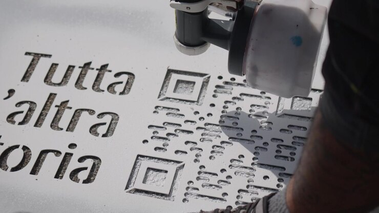 Yksityiskohtainen lähikuva spraymaalauksesta geometrisen sapluunan läpi, jossa on typografiaa ja QR-koodi, esitellen nykyaikaisen katutaiteen luomisprosessia.