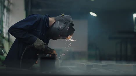 portrait a man welder works in a factory and welds steel metal parts in slow motion. sparks fly