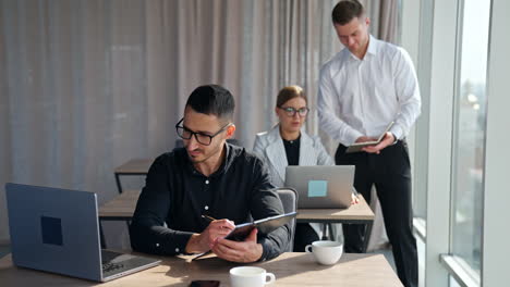 male manager standing at the desk of female employee checking the data in his notebook. male brunet colleague focused on the screen of his laptop.