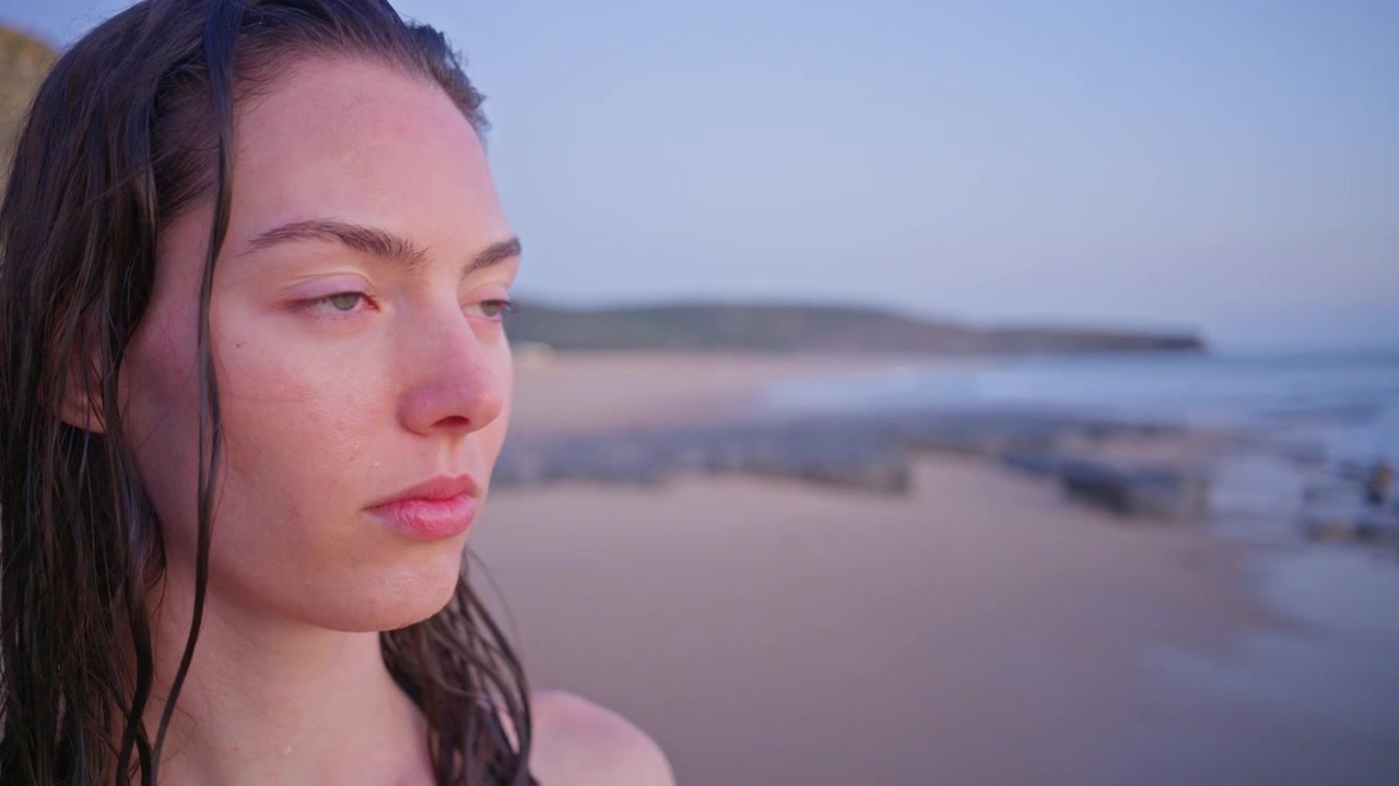 Close up portrait of a young woman with wet hair looking toward the ocean after swimming, with soft natural light and a calm cinematic beach lifestyle mood.