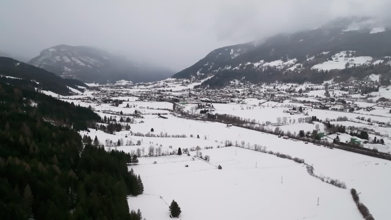 vista aerea di un campo innevato in una valle di montagna nebbiosa con foresta sulla collina