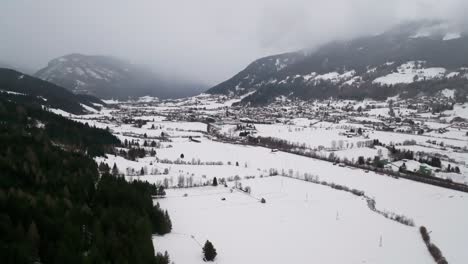 Aerial-view-of-snowy-field-in-foggy-mountain-valley-with-forest-on-hillside