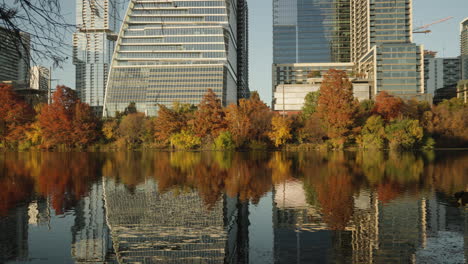 Wunderschöne-Bäume-Und-Gebäude-In-Der-Innenstadt-Mit-Spiegelung-Im-Wasser-Des-Sees-Während-Des-Herbstsonnenuntergangs-Mit-Hübschen-Farben-In-Den-Baumblättern