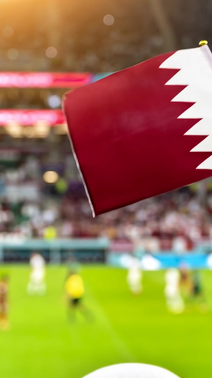 Video verticale: Un uomo in thobe e ghutra sugli spalti guarda una partita mentre la bandiera del Qatar entra da destra.