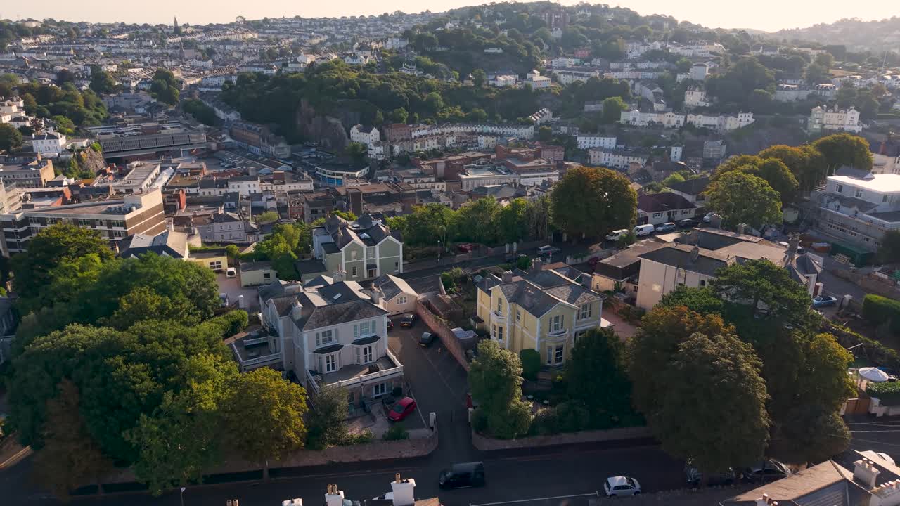 Graceful ascending drone shot over Torquay's rolling hills at dawn. Rising movement reveals hotels, residential areas and houses beyond the hillcrest with beautiful long summer shadows