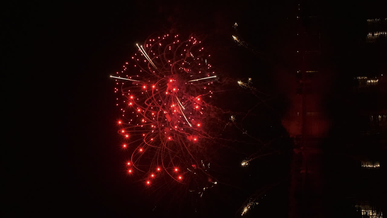 formato vertical: fuegos artificiales estallan en el cielo nocturno oscuro sobre el agua tranquila