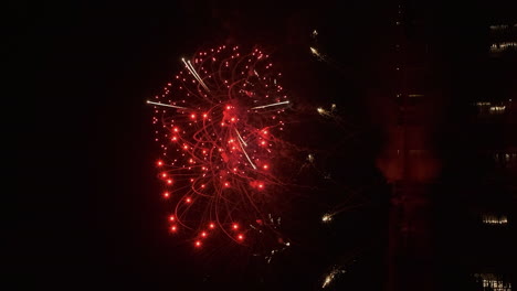 Vertical-format:-Fireworks-erupt-in-dark-night-sky-over-calm-water