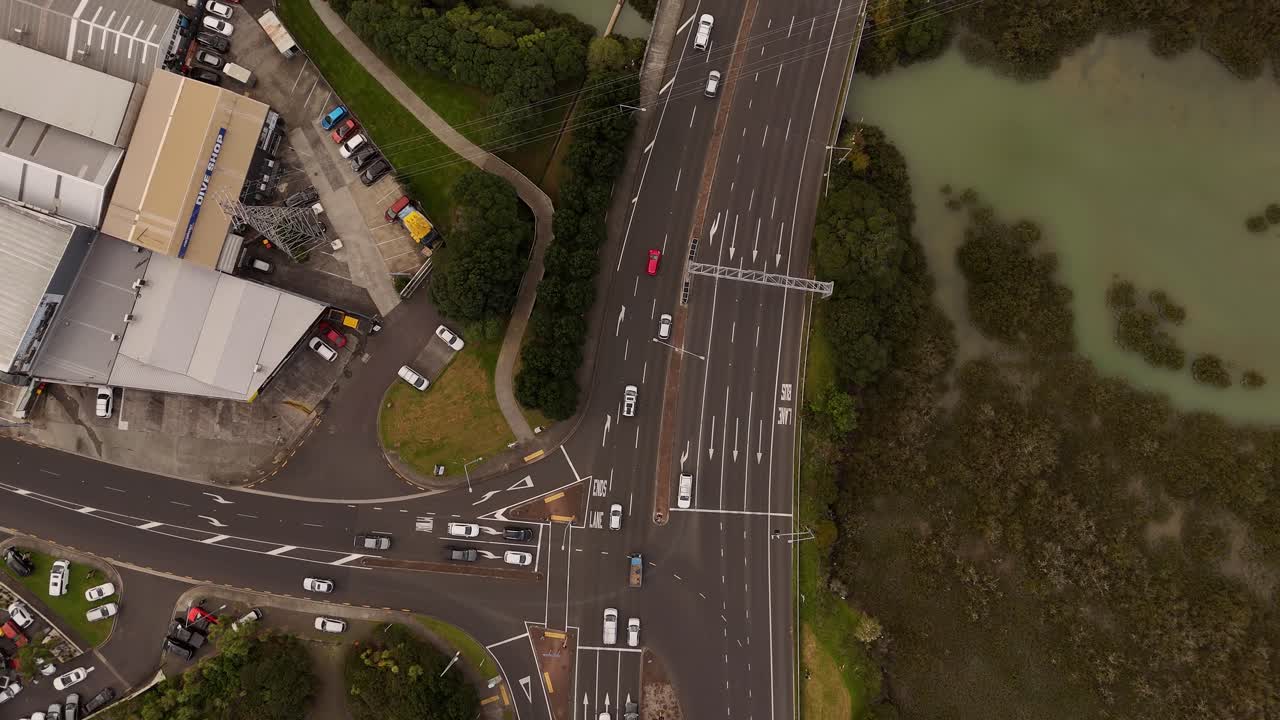 Traffic scene on junction of highway in Auckland, nz. Cloudy summer day at sunset. Aerial top down. Driving cars turning into road. Grass fields and bush and lake at takapuna area