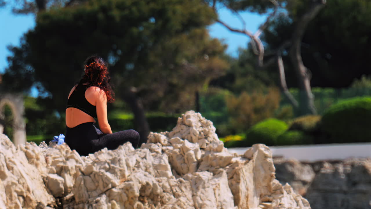 Woman wearing a black sportswear set resting on the rocks with trees on the background