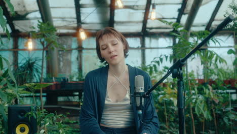 female performer singing in mic and playing synthesizer in greenhouse
