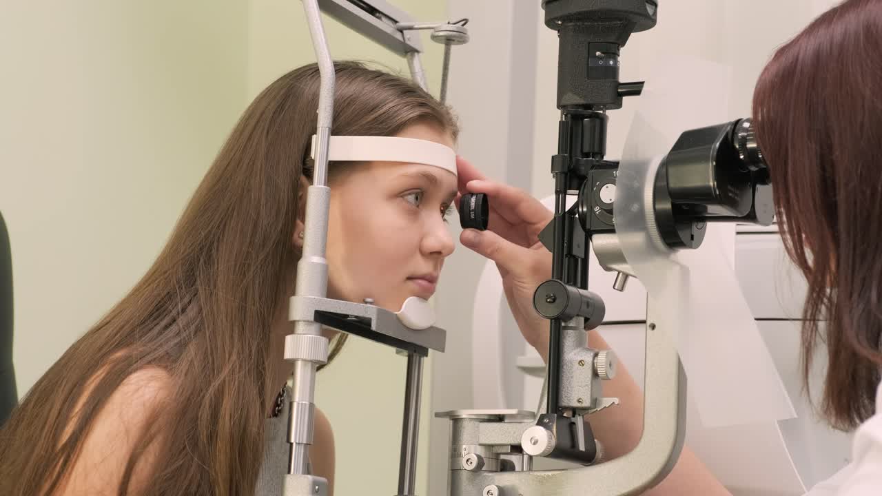 Ophthalmologist check eyesight of young teen with modern equipment. Doctor checking eyes with biomicroscope device. Dolly shot of female doctor examining eye structure with help of medical equipment