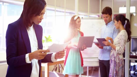 Businesswoman-checking-documents-while-coworker-interacting-in-background