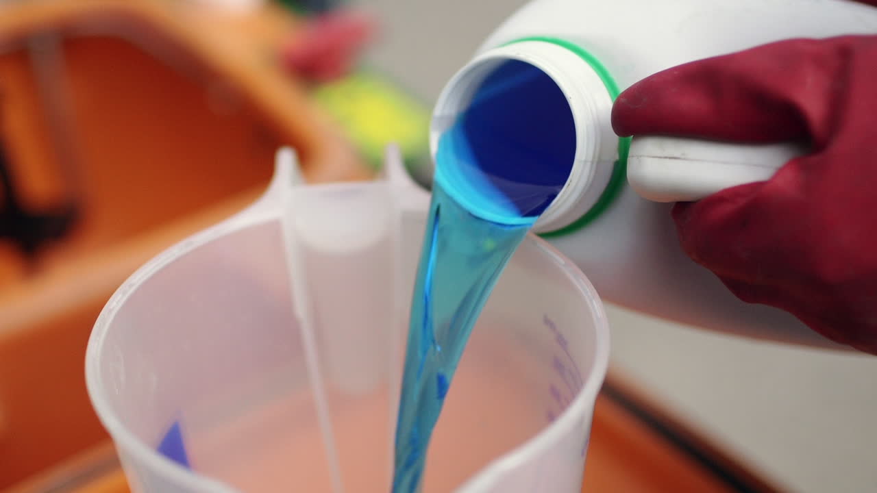 Farmer preparing field sprayer with plant protection products before heading to the field. Pesticide being poured into measuring cup.