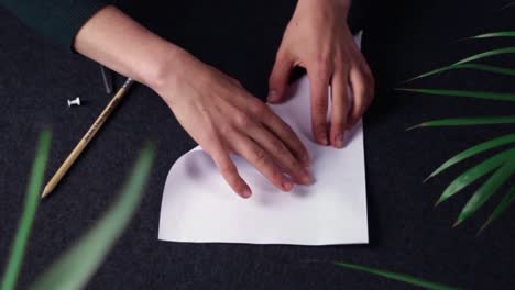 static view of caucasian hands folding a blank sheet of a four paper on a black table to make a pinwheel