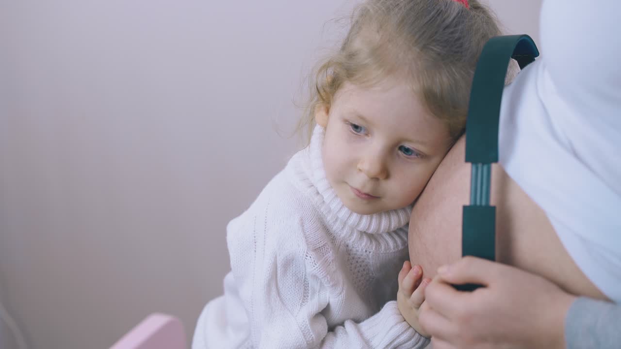 девочка надевает наушники, слушая реакцию ребенка в животе мамы.