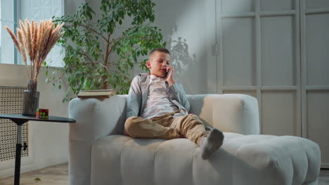 schoolboy calls mother on phone sitting on comfortable sofa