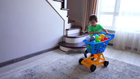 cute baby boy pushing a toy shopping cart filled with colorful balls. little kid having fun at home.